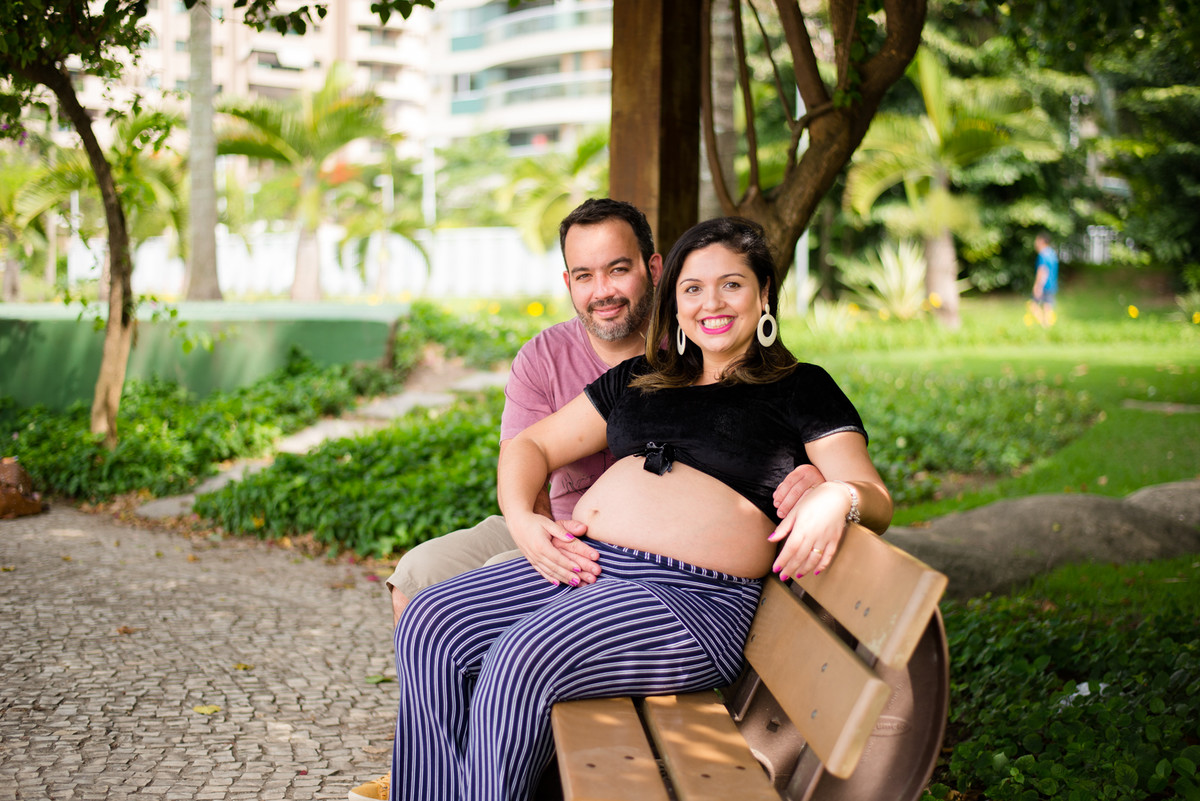 papais felizes com as mãos no seu barrigão registrado pelo fotógrafo de gestante Nós Dois Fotografia na Barra da Tijuca RJ num belo jardim de fundo