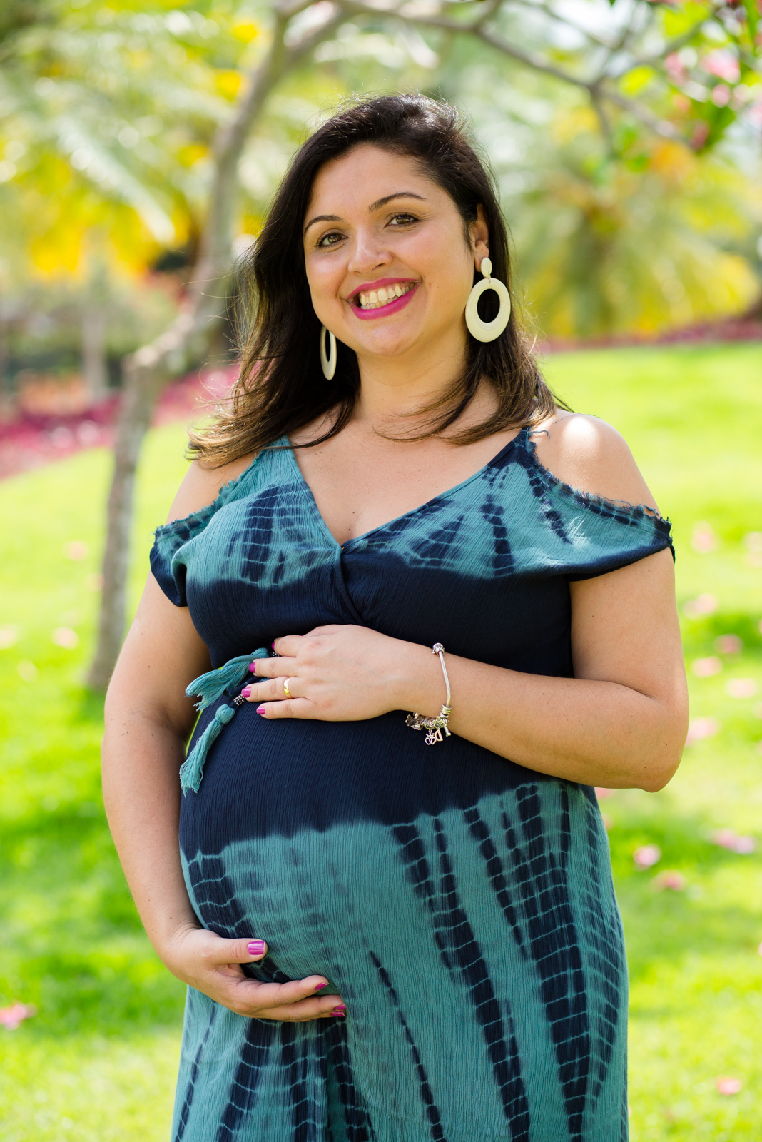 Mamãe feliz com as mãos no seu barrigão registrado pelo fotógrafo de gestante Nós Dois Fotografia na Barra da Tijuca RJ num belo jardim de fundo