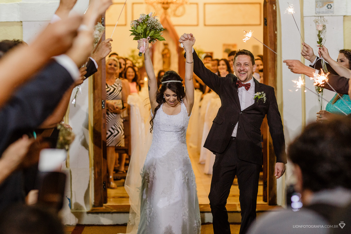 Felizes e empolgados os noivos saem da igreja sorrindo e pulando