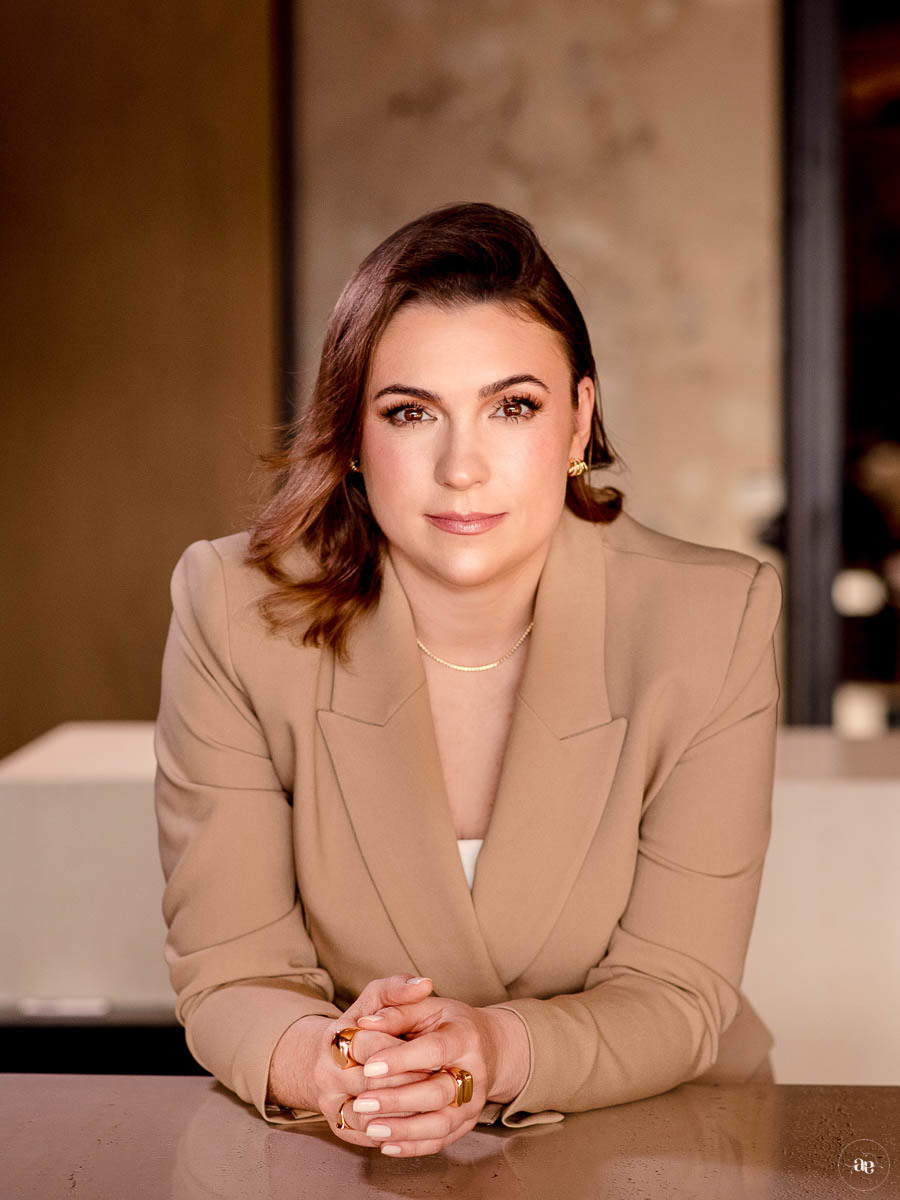 Fotografia de posicionamento da arquiteta Suellen Faccio em blazer bege, com olhar direto para a câmera e expressão serena, transmitindo confiança e autoridade profissional.