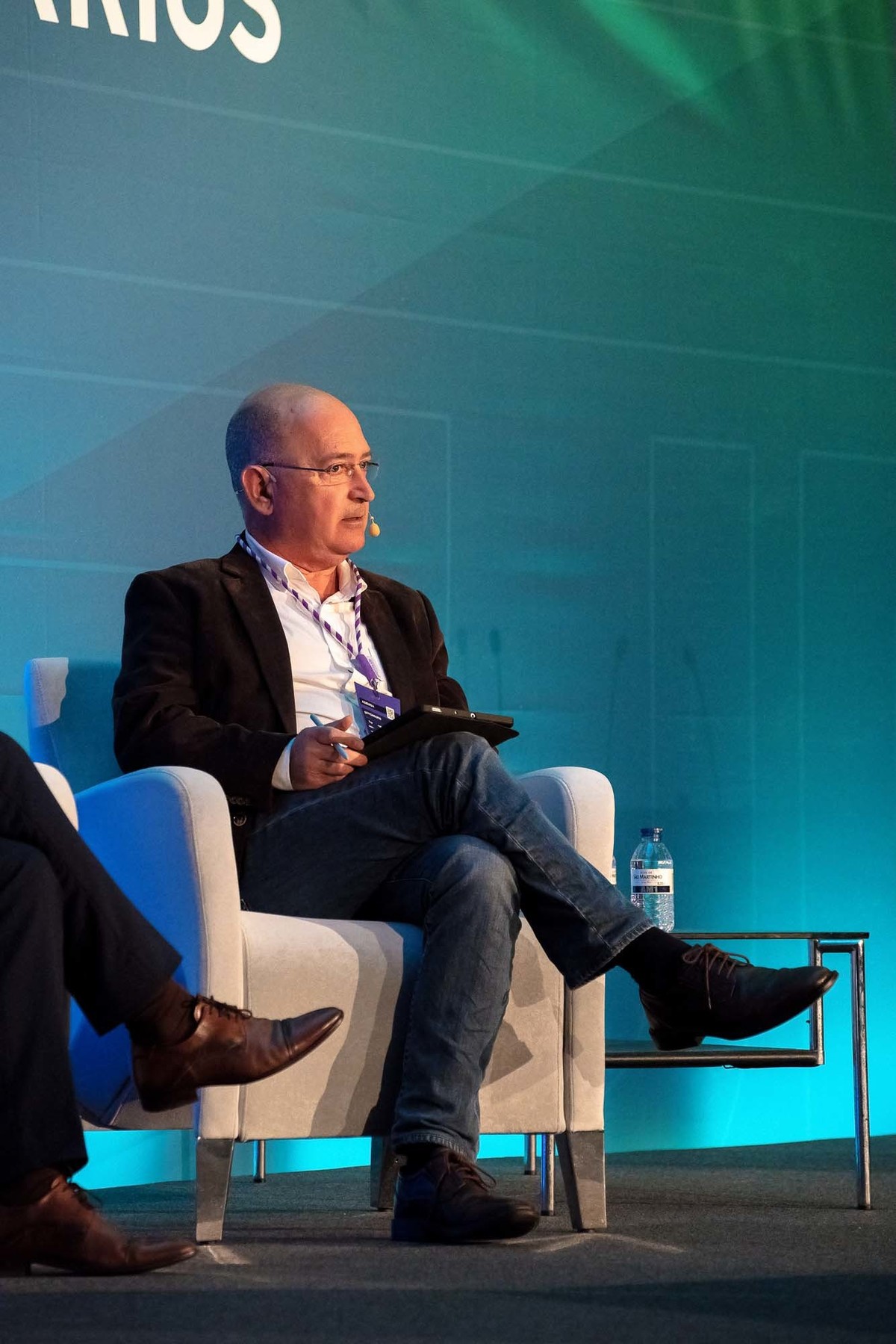 Fotografia lateral do orador principal com o logótipo do evento no fundo.