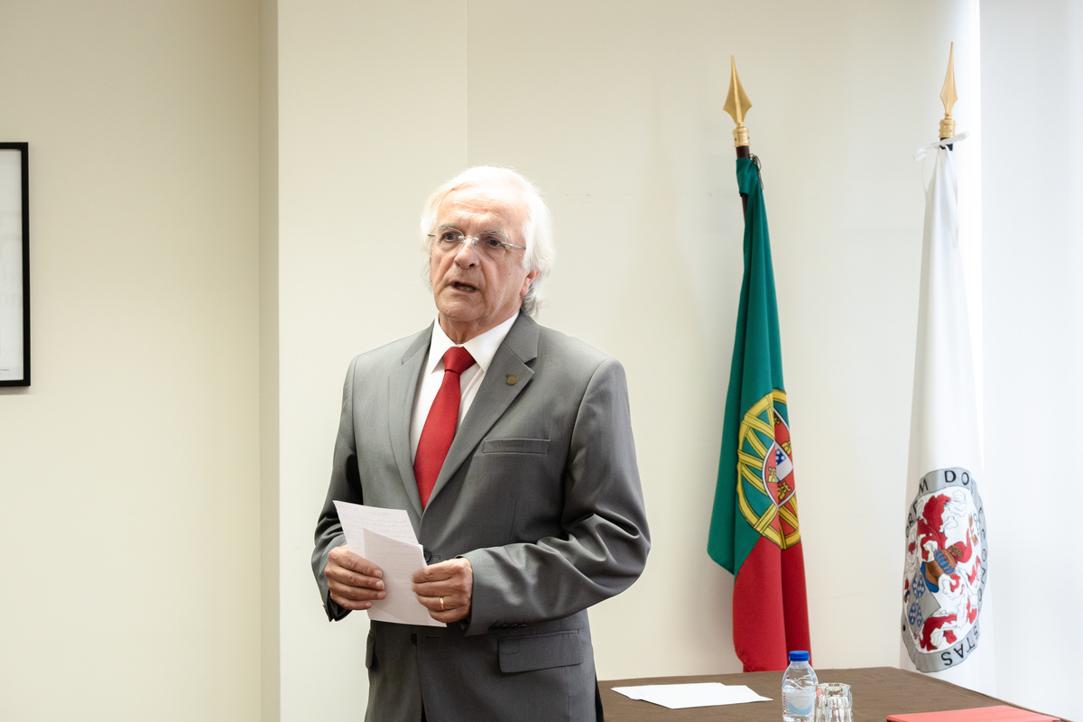Orador masculino a discursar com a bandeira de Portugal ao fundo