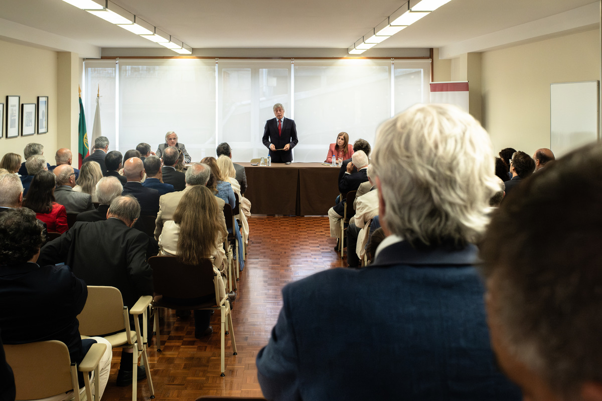 Vista geral da sala com convidados sentados e foco no ambiente institucional