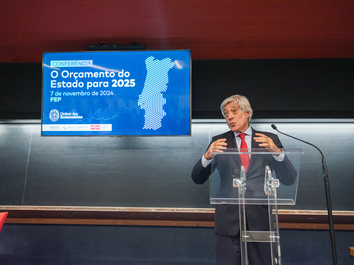 Orador em pé com expressão confiante durante apresentação financeira