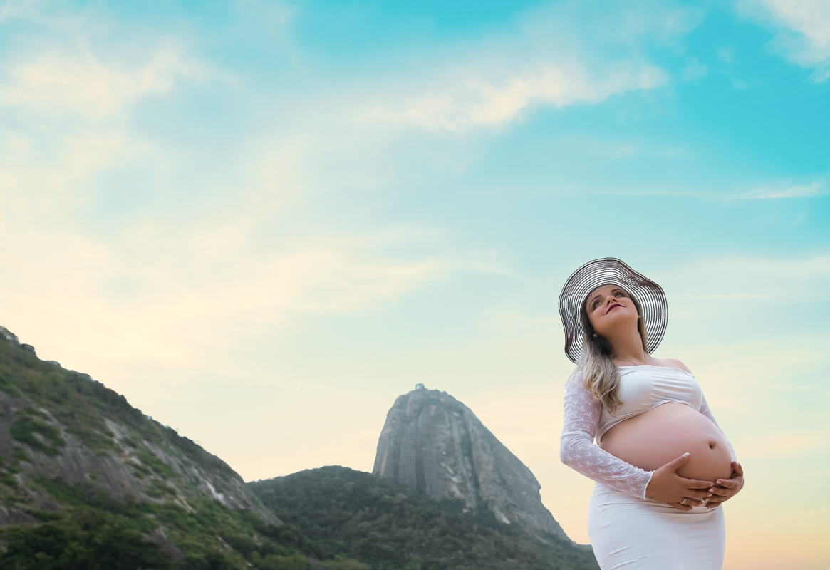 Fotografia de gravida na praia usando chapéu 
