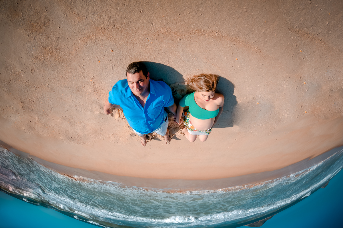 Ensaio gestante deitada na areia junto com esposo