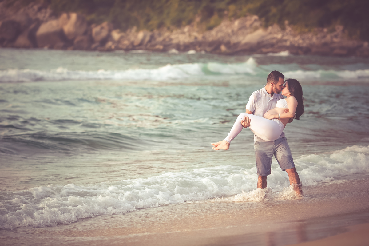 Gestante no colo do marido na prainha