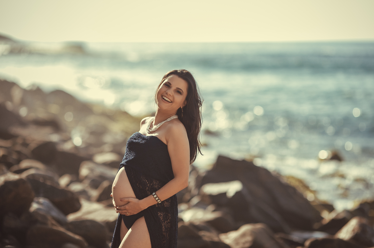 Gestante colocando mão na barriga e pedras no fundo em Praia do Rio de Janeiro