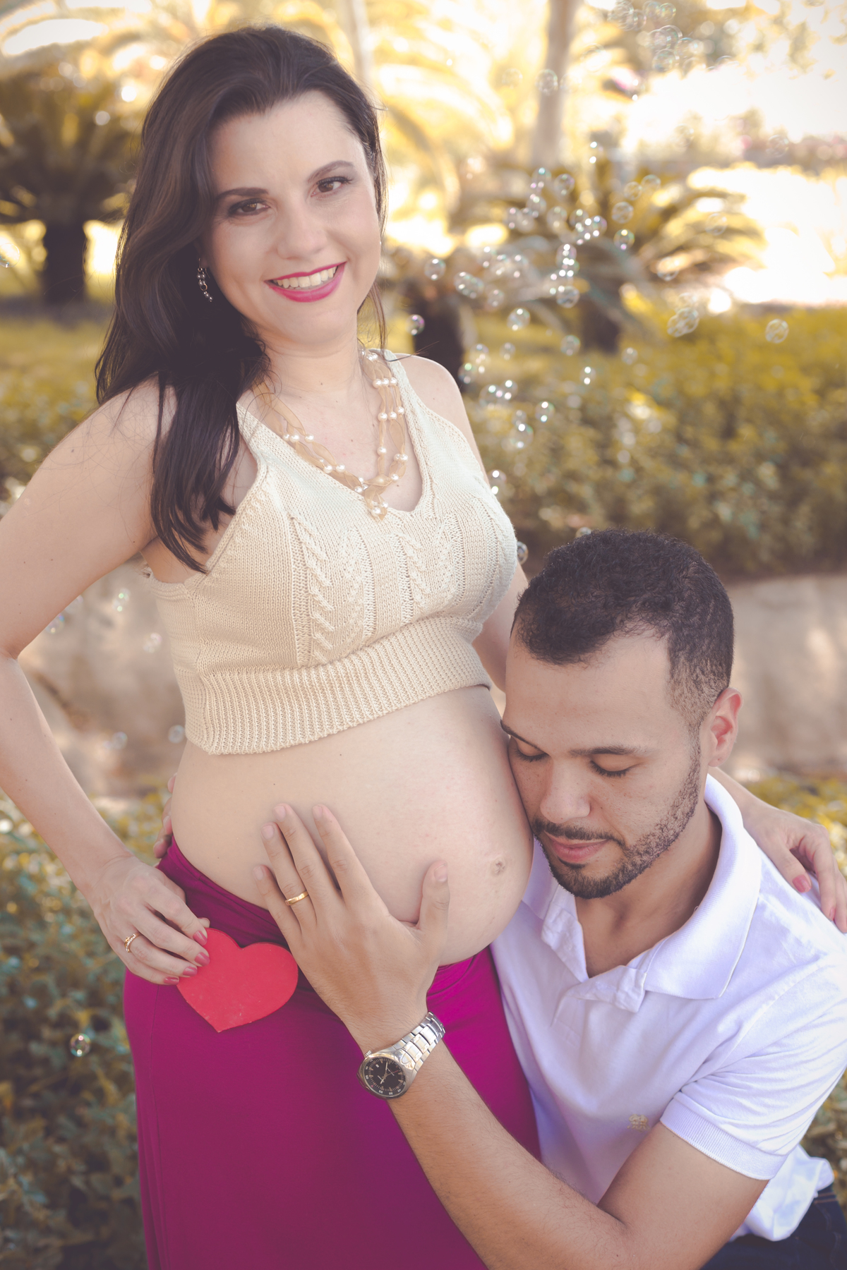 Ensaio fotográfico externo pai ouvindo a barriga da gestante com os olhos fechados