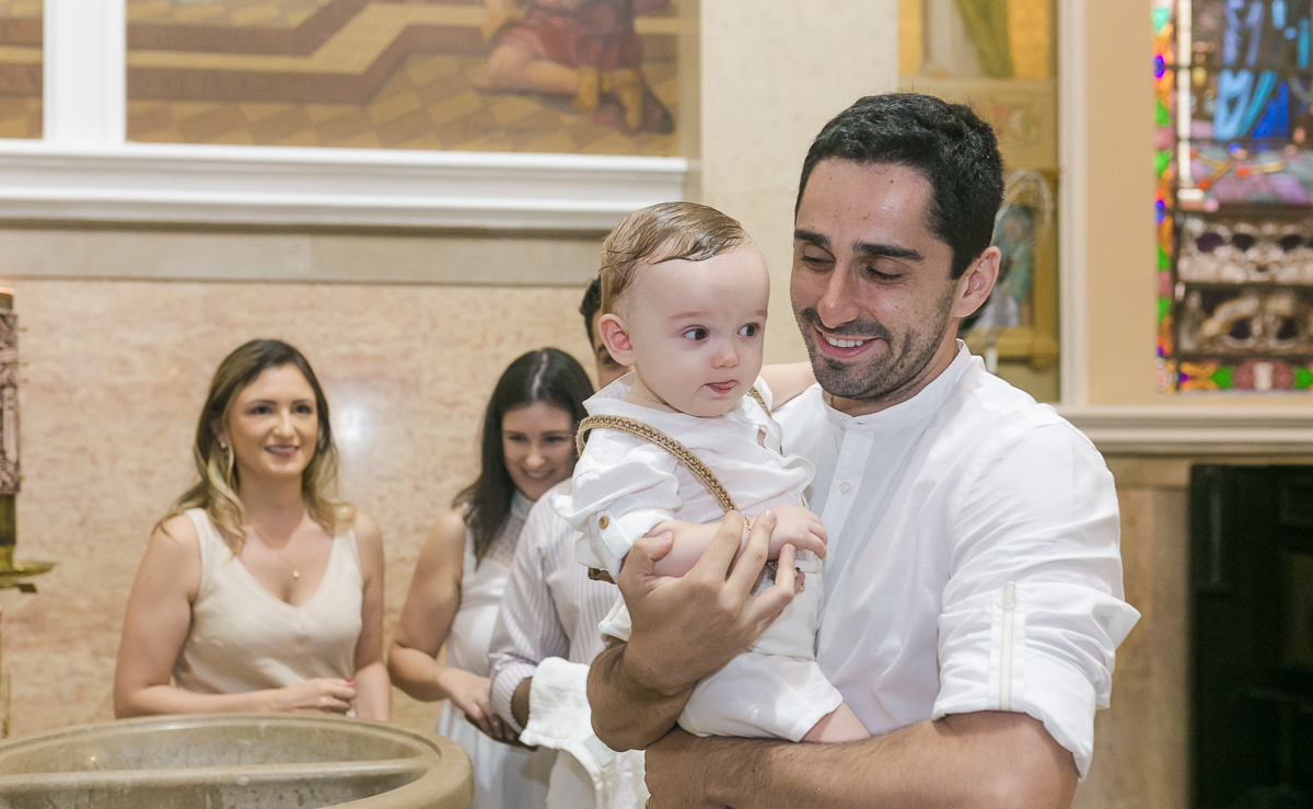 Pai segurando filho apos seu batizado na Paróquia São Paulo Apostolo