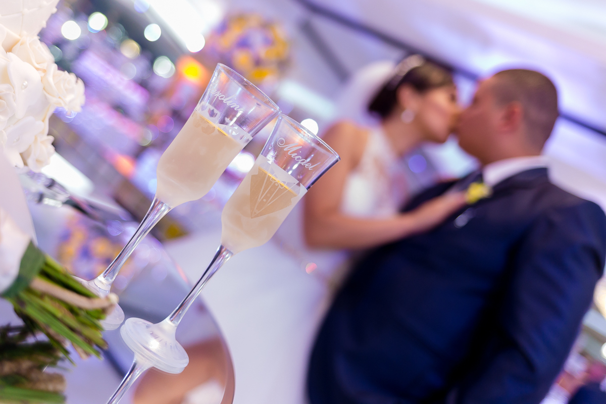 Taças   em cima da mmesa e noivos se beijando ao fundo em Casa de festas jardim do casarão