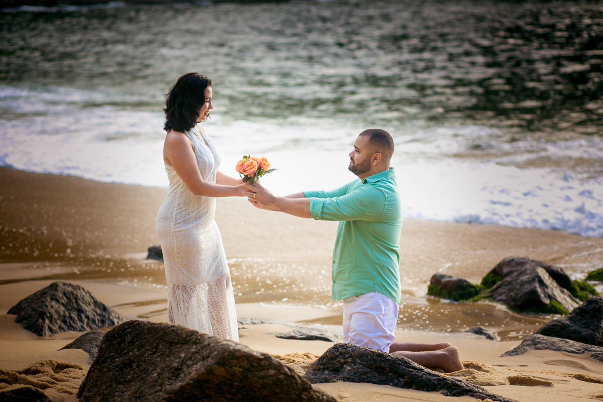 Ensaio casal noivo ajoelhado na praia da Urca oferecendo buquê a sua noiva