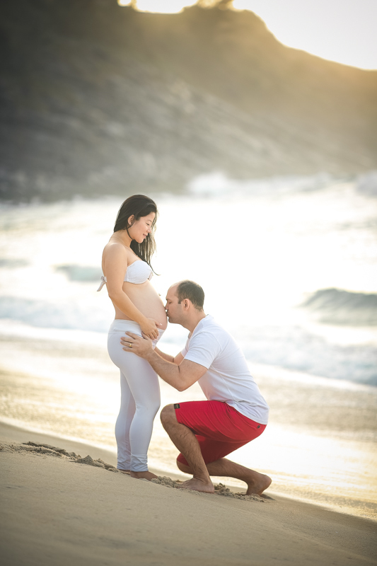 Ensaio de gestante pai ajoelhado beijando barriga em Grumari-RJ