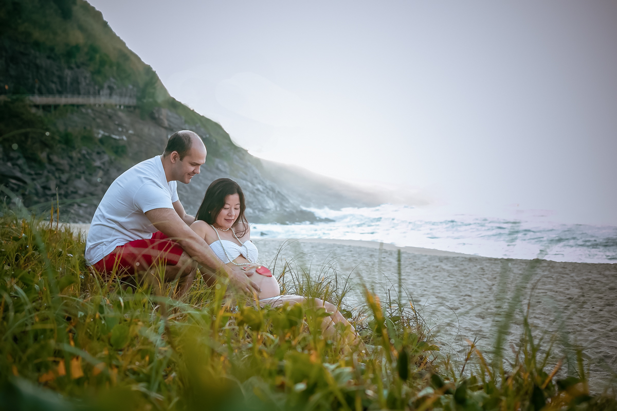 Gestante sentada na grama e ao fundo o mar na pria de Grumari-RJ