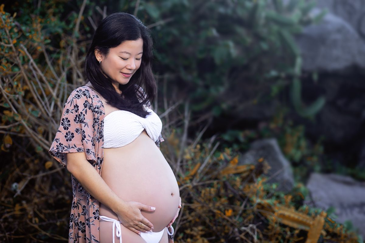 Gestante usando biquíni branco e segurando a barriga em ensaio fotográfico-Grumari