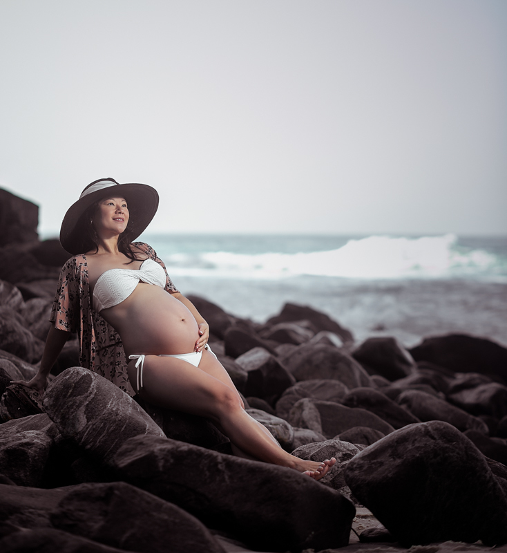 Gestante sobre as pedras usando chapéu preto em ensaio na praia-Grumari-RJ 