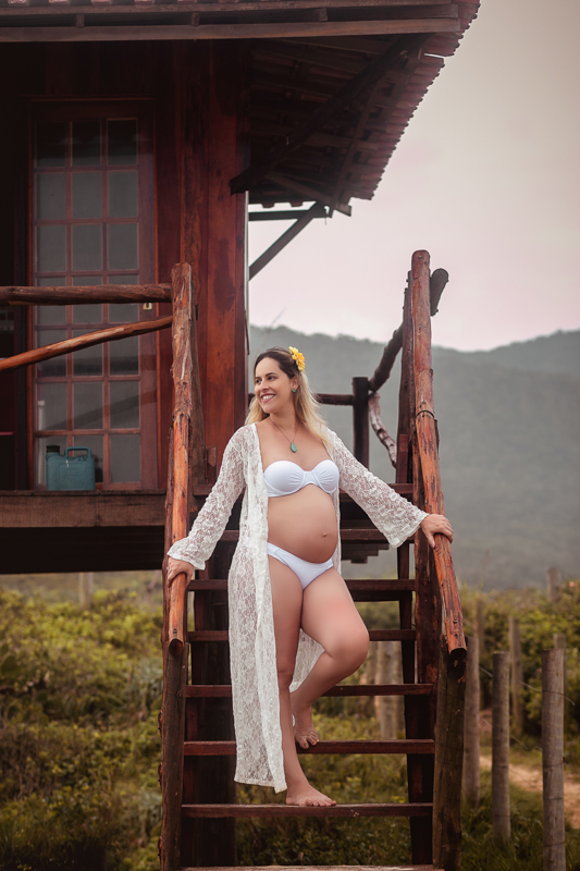 Fotografia de gestante na praia com flor amarela na cabeça em Grumari/RJ