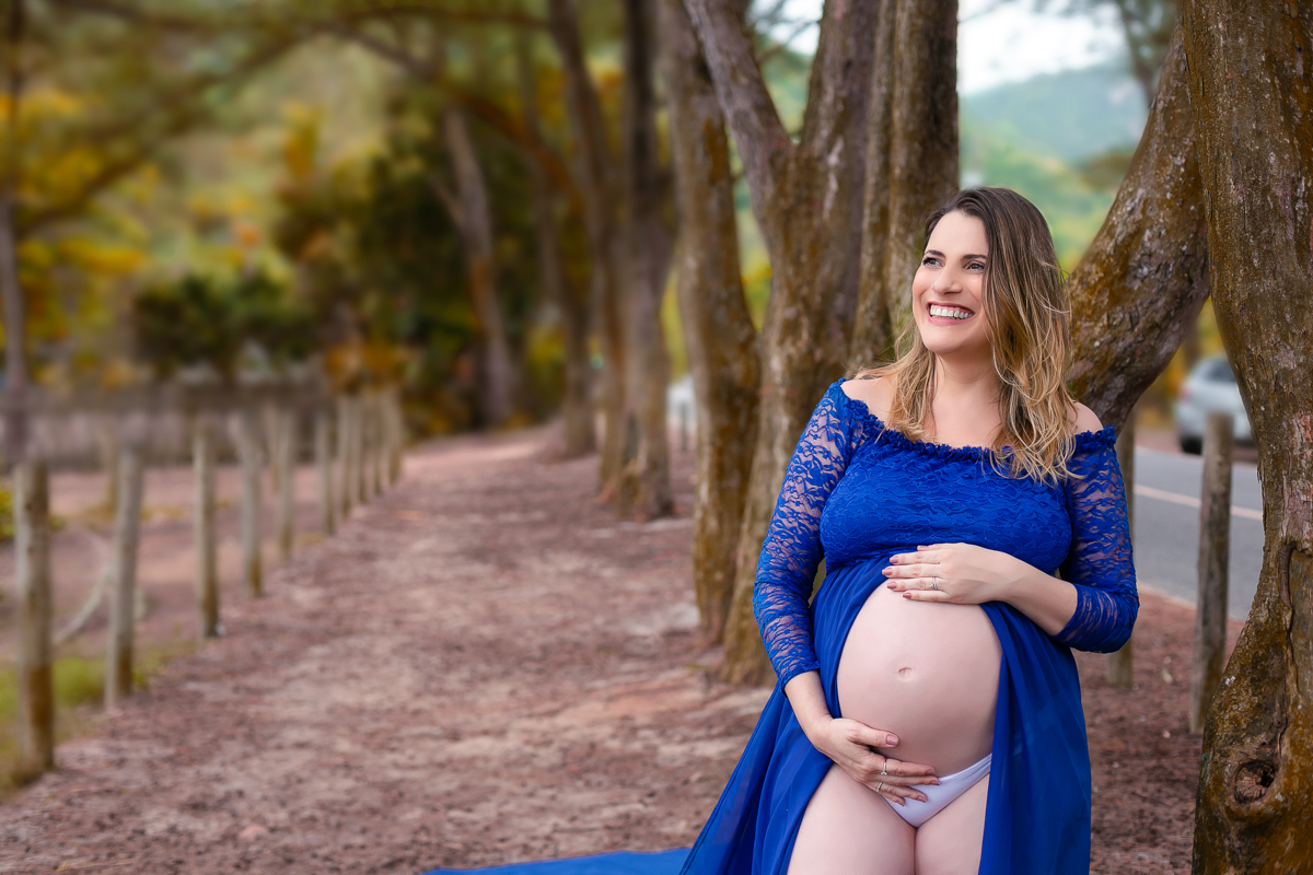 Ensaio externo de gestante ele encostada nas árvores em seu ensaio fotográfico em Grumari/RJ