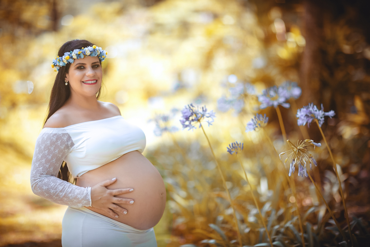 Ensaio externo de gestante usando roupa branca e enfeite de rosas na cabeça em Parque Crémerie/Petrópolis