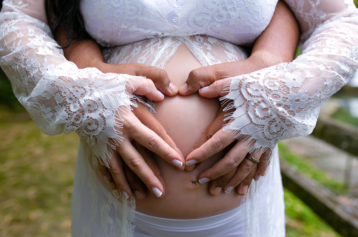 Book fotográfico de gestante junto com seu esposo fazendo um coração na barriga em Parque Crémerie/Petrópolis