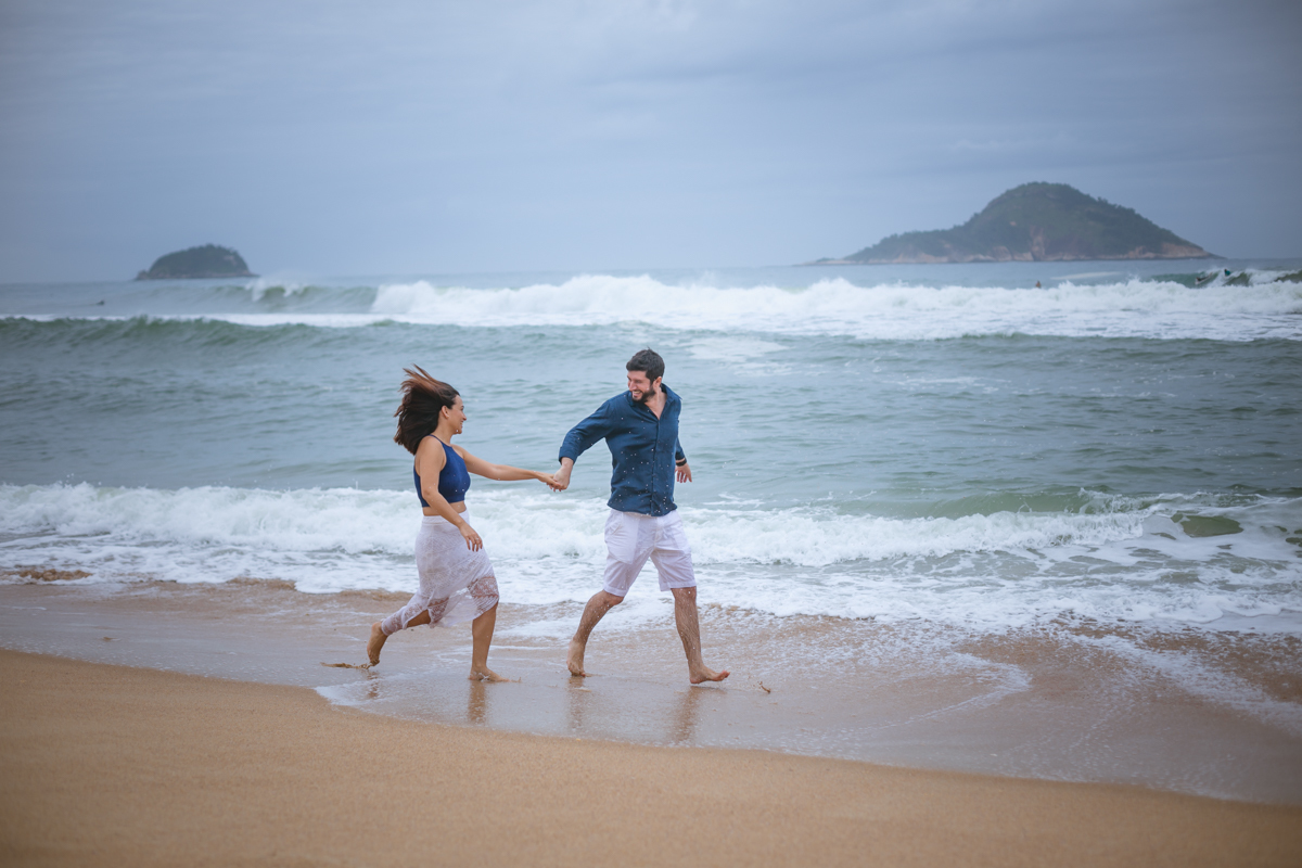 Casal brincando, correndo na areia em seu pré-wedding em Grumari/RJ 