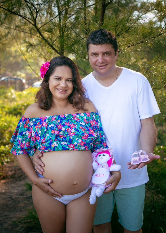Ensaio de gestante externo ela segurando boneca de pano com nome Alice e papai com sapatinho rosa nas mãos/Gruamri-RJ
