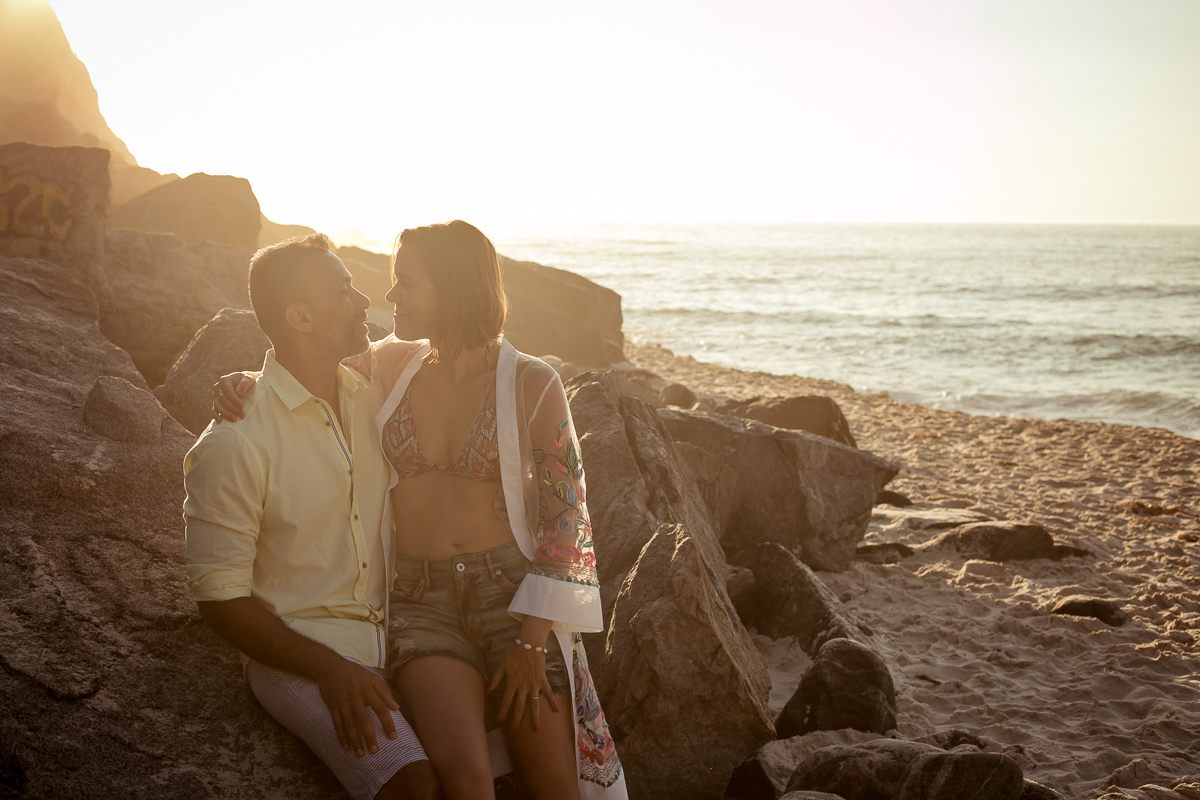 Casal sentado sobre a pedra em ensaio romântico na prainha/RJ