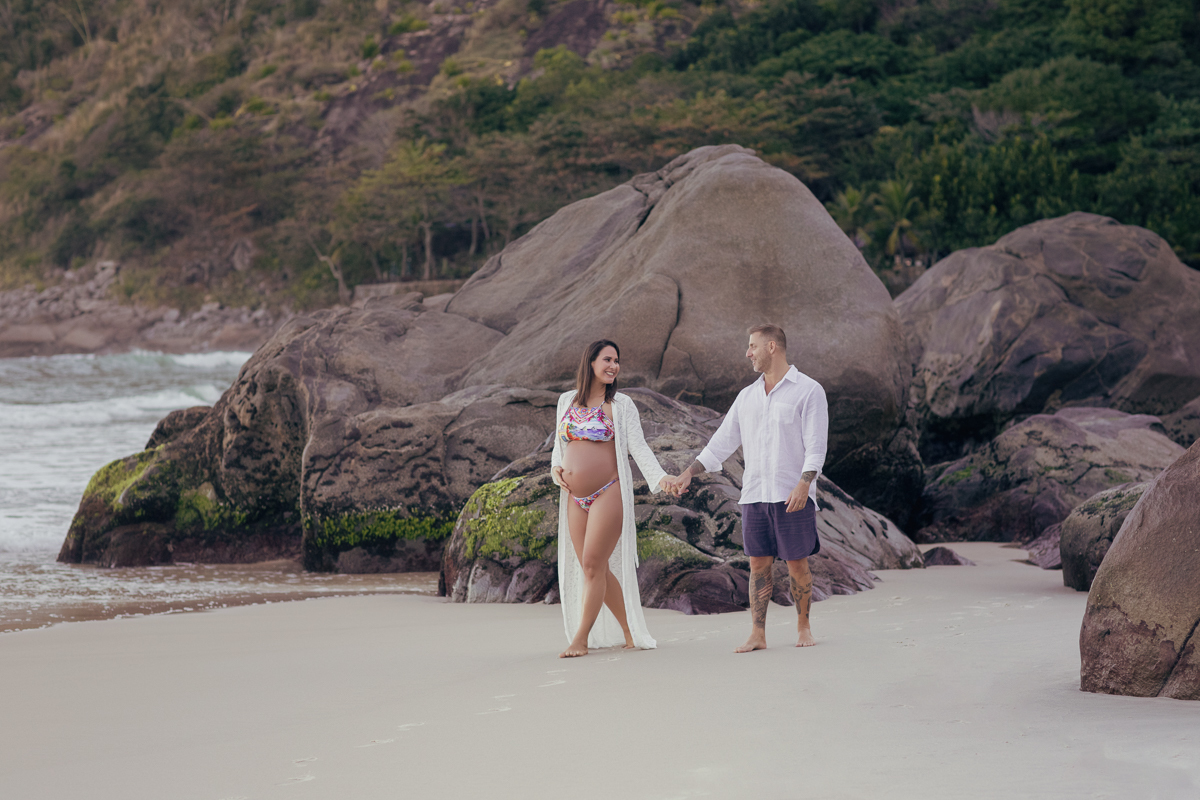 gestante caminhando na praia de mãos dadas com seu esposo em ensaio fotográfico-RJ
