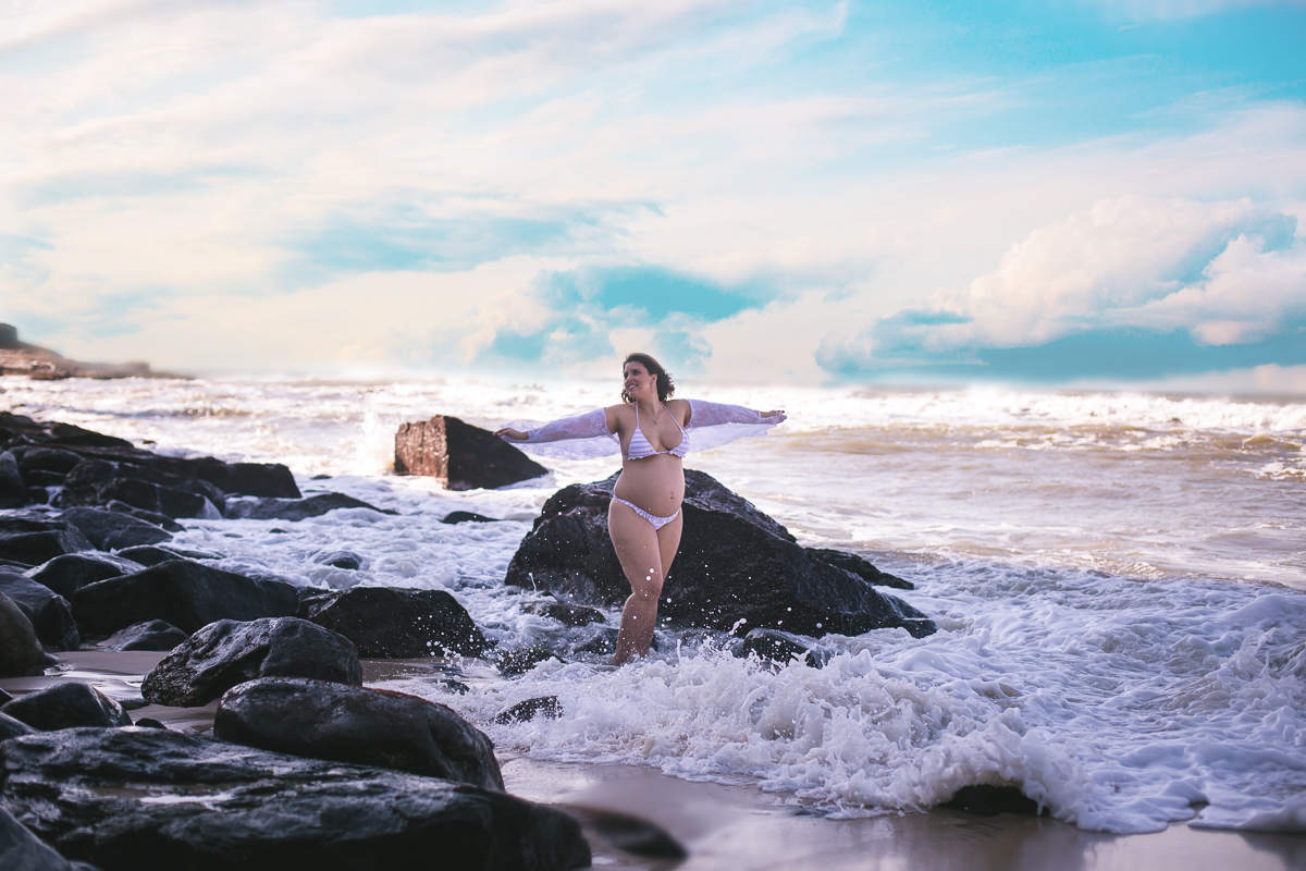 gestante em ensaio externo de braços abertos ao fundo  mar quebrando as ondas em prainha/RJ
