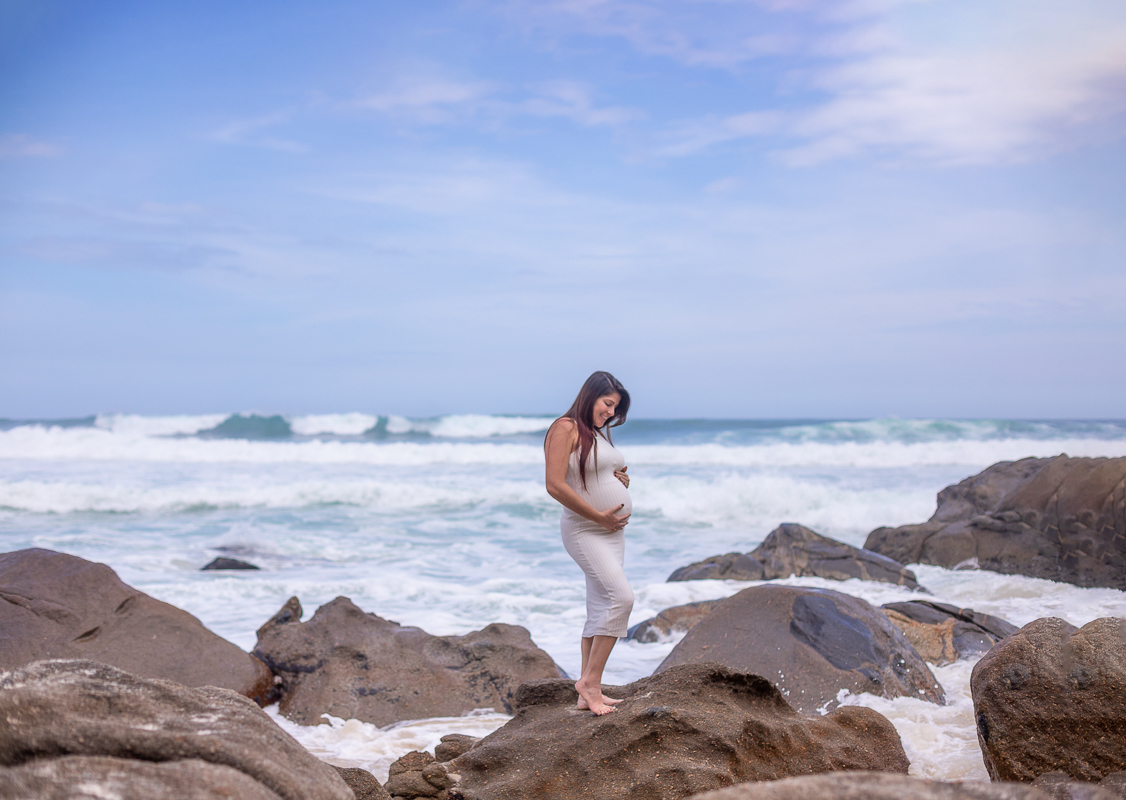 gestante em pedras com a mão na barriga em ensaio externo-praia-rj