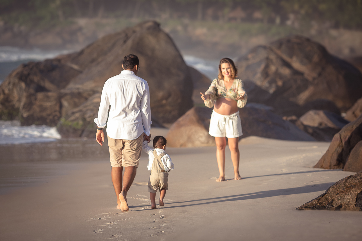 pai caminhando na areia com o filho ao encontra da mãe gestante-ensaio externo-rj