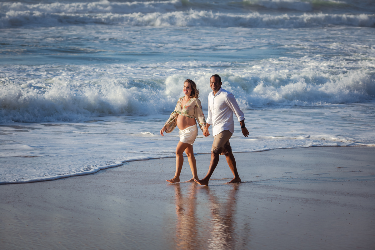 gestante caminhando de mãos dados junto com esposo na pra em seu book fotográfico-prainha rj