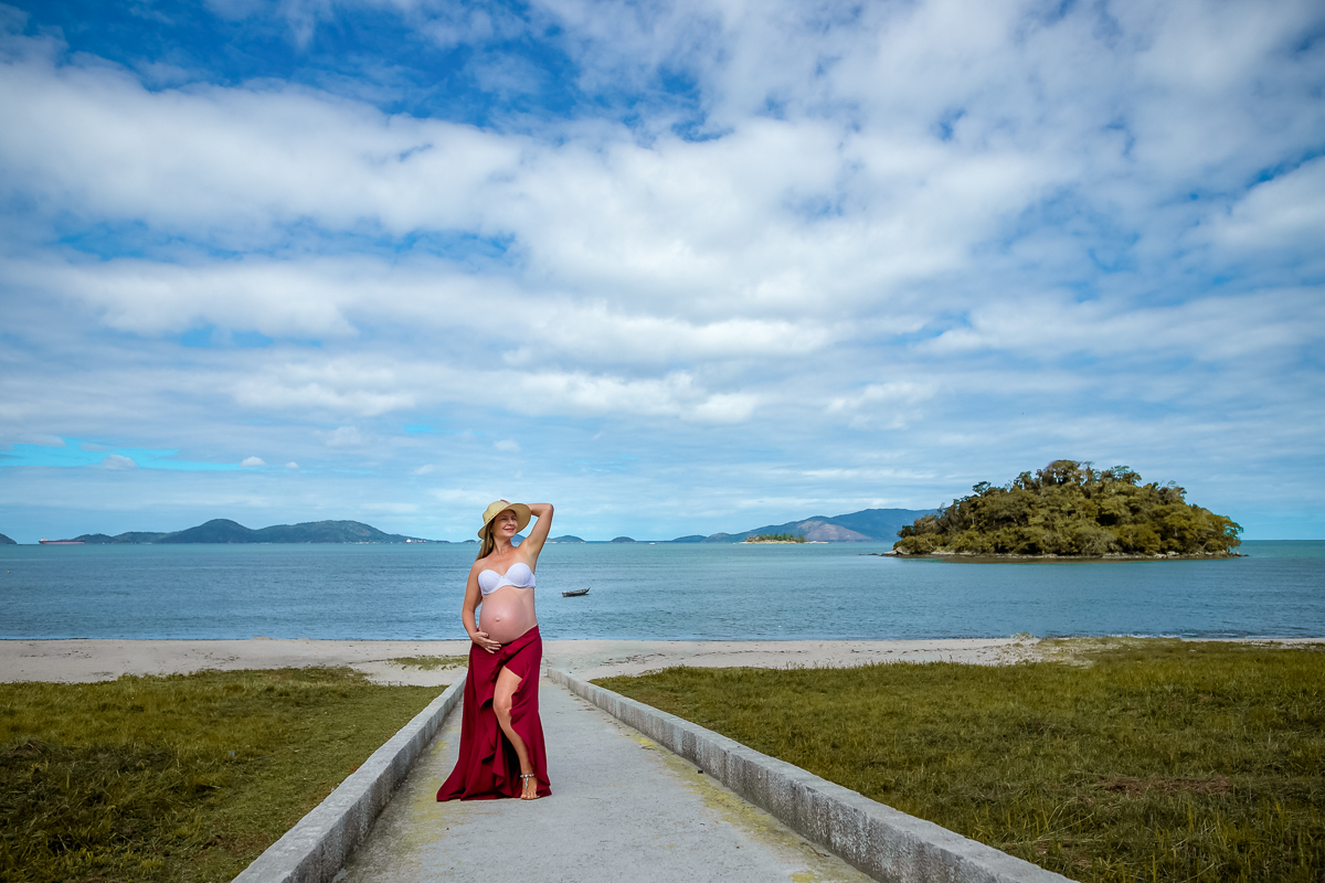 gestante fazendo pose  em praia ao fundo céu azul e mar-ensaio externo-Mangaratiba-Sahy-RJ