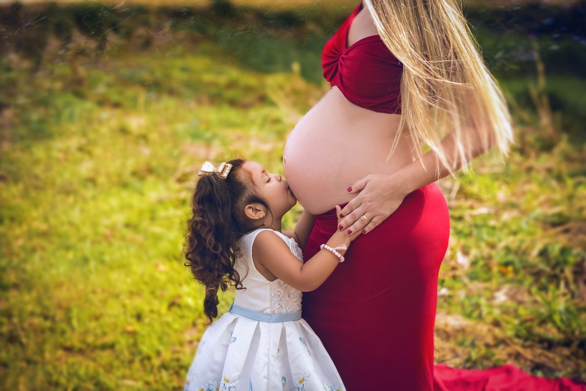 filha beijando barriga de sua mãe gestante em ensaio fotográfico externo