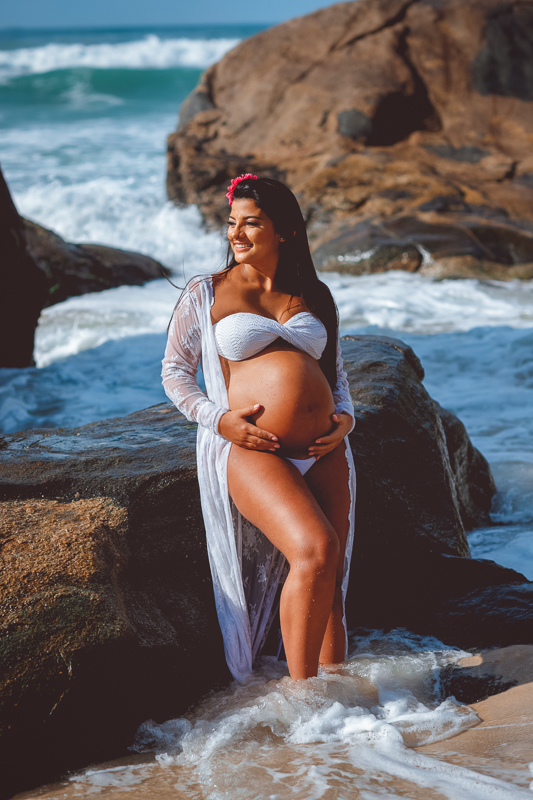 ensaio fotografico-gestante segura a barriga ao fundo-pedras  mar