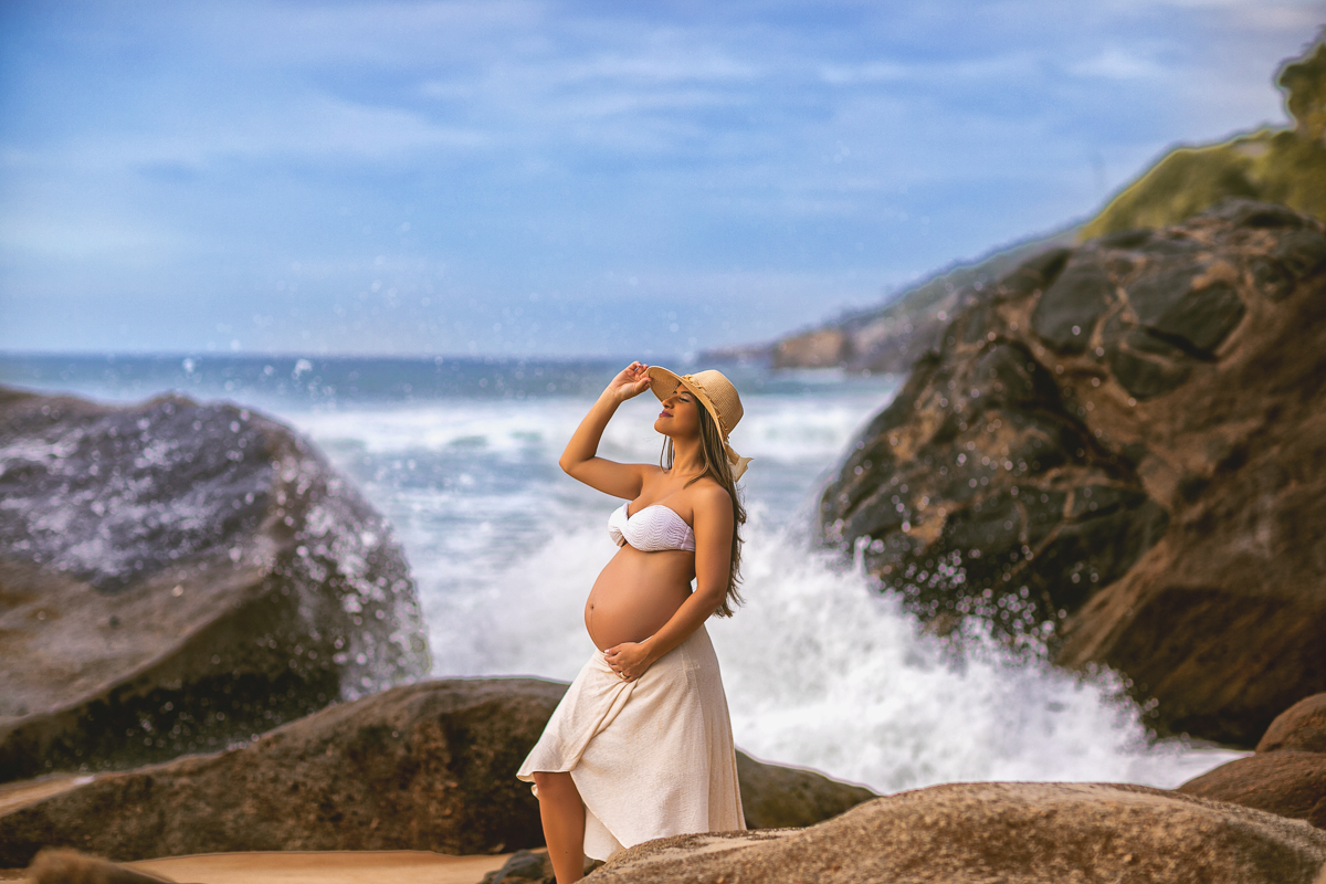 mar batendo nas pedras ao fundo e gestante fazendo pose em seu ensaio fotográfico-prainha-rj