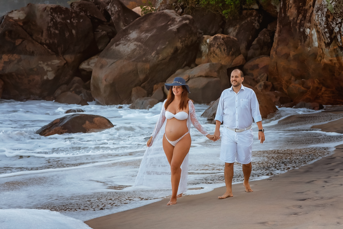 gestante caminha de mãos dados com esposa na praia-em seu ensaio fotográfico