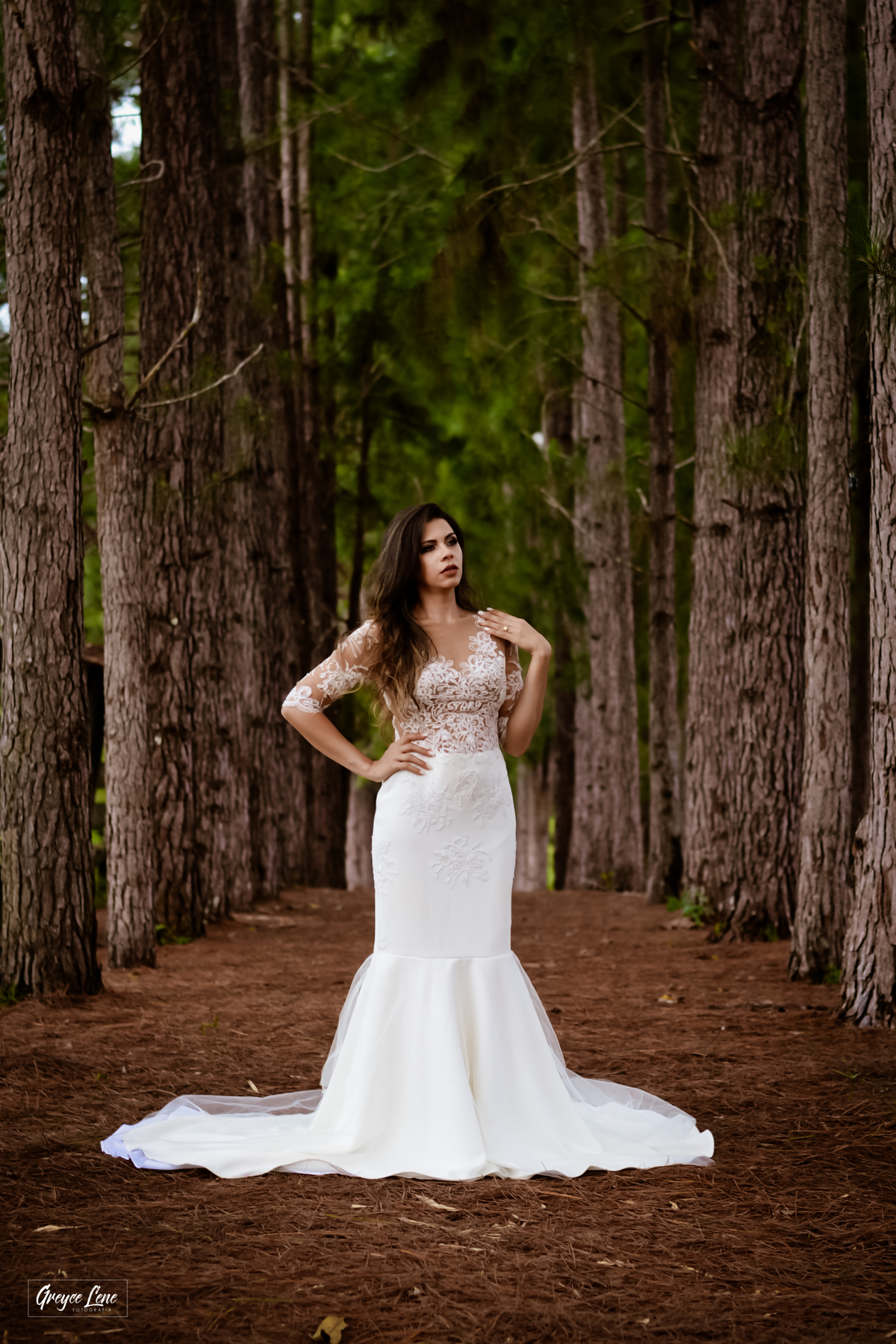 noiva sozinha corpor inteiro em meio aos pinheiros com uma mão na cintura e outra no ombro olhando o horizonte 