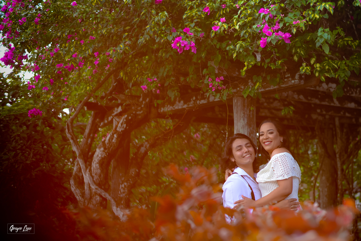casal abraçado sorrindo ensaio fotográfico embaixo do pergolado florido
