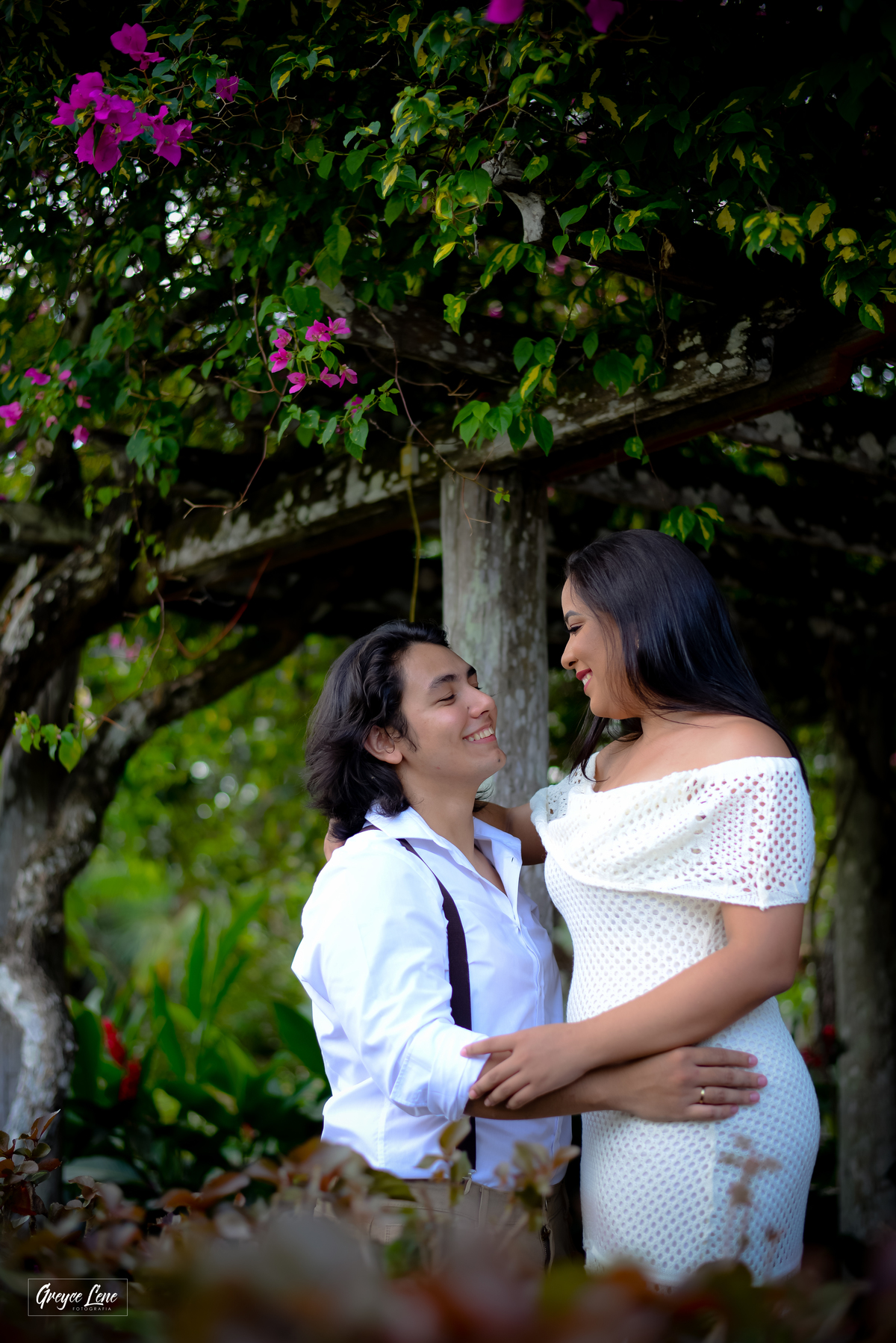 casal abraçado sorrindo olhando um para o outro ensaio fotográfico embaixo do pergolado florido