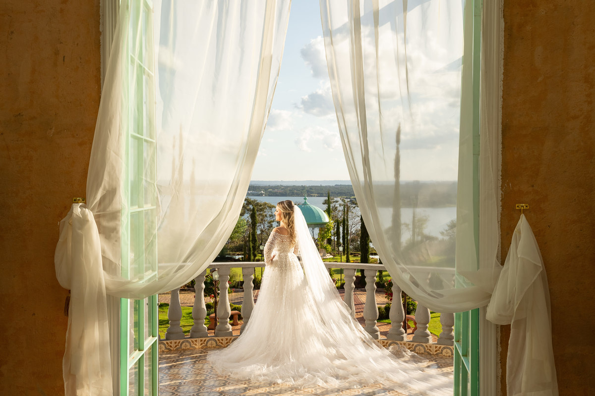 De dentro do Pallazo nosso artista Sandro Andrade faz no detalhe as cortinas e na frente está a nossa linda noiva com o gazebo do giardino de fundo, dono de uma criatividade e conhecimento único, Sandro trouxe luz natural e artificial na mesma fotografia,