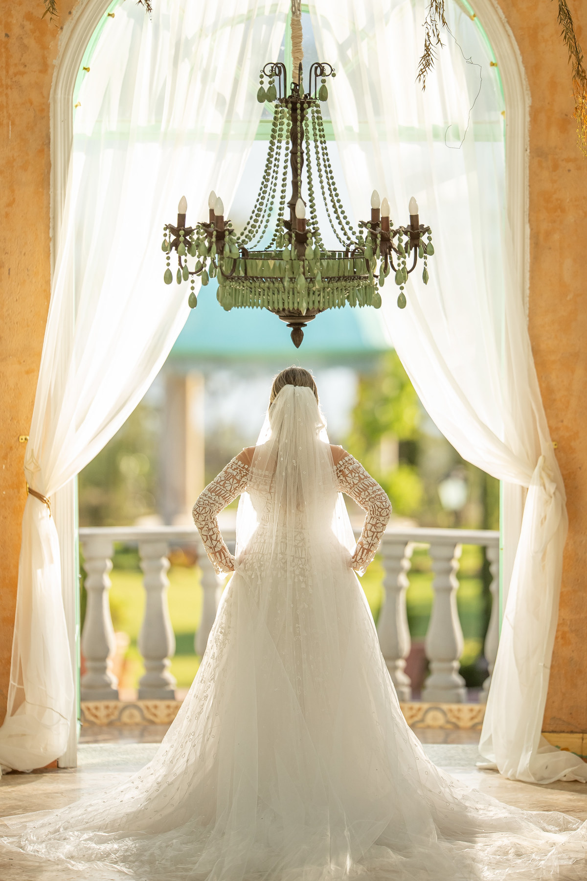 Com o lustre acima da cabeça Manú está de costas, com as mãos na cintura, olhando para o Giardino, tudo em um lindo retrato colorido. 