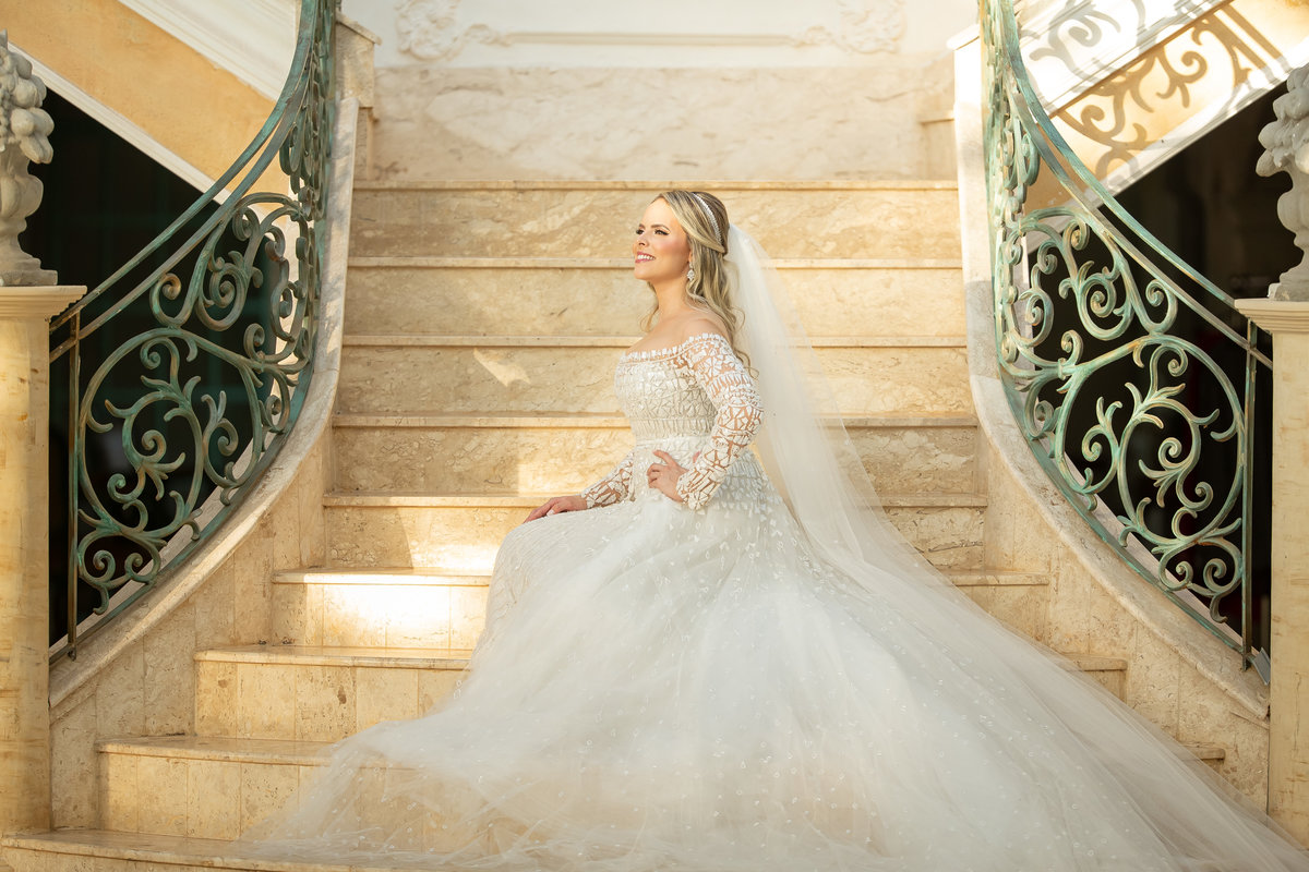 Manú está sentada na escadaria interna da Villa Giardini, com o sol batendo em rosto, linda e plena, muito bem produzida, um lindo retrato de noiva.