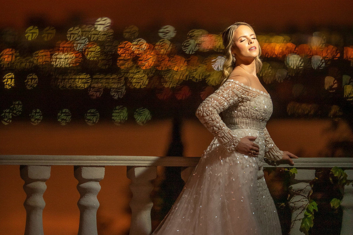 Uau...que linda esta fotografia, a noiva está linda, com os olhos fechados, a mão na cintura, uma luz linda artificial encaixada em seu rosto, trazendo luz e sombra e ao fundo o lago refletindo o céu  e formando bokes coloridos e riscados.