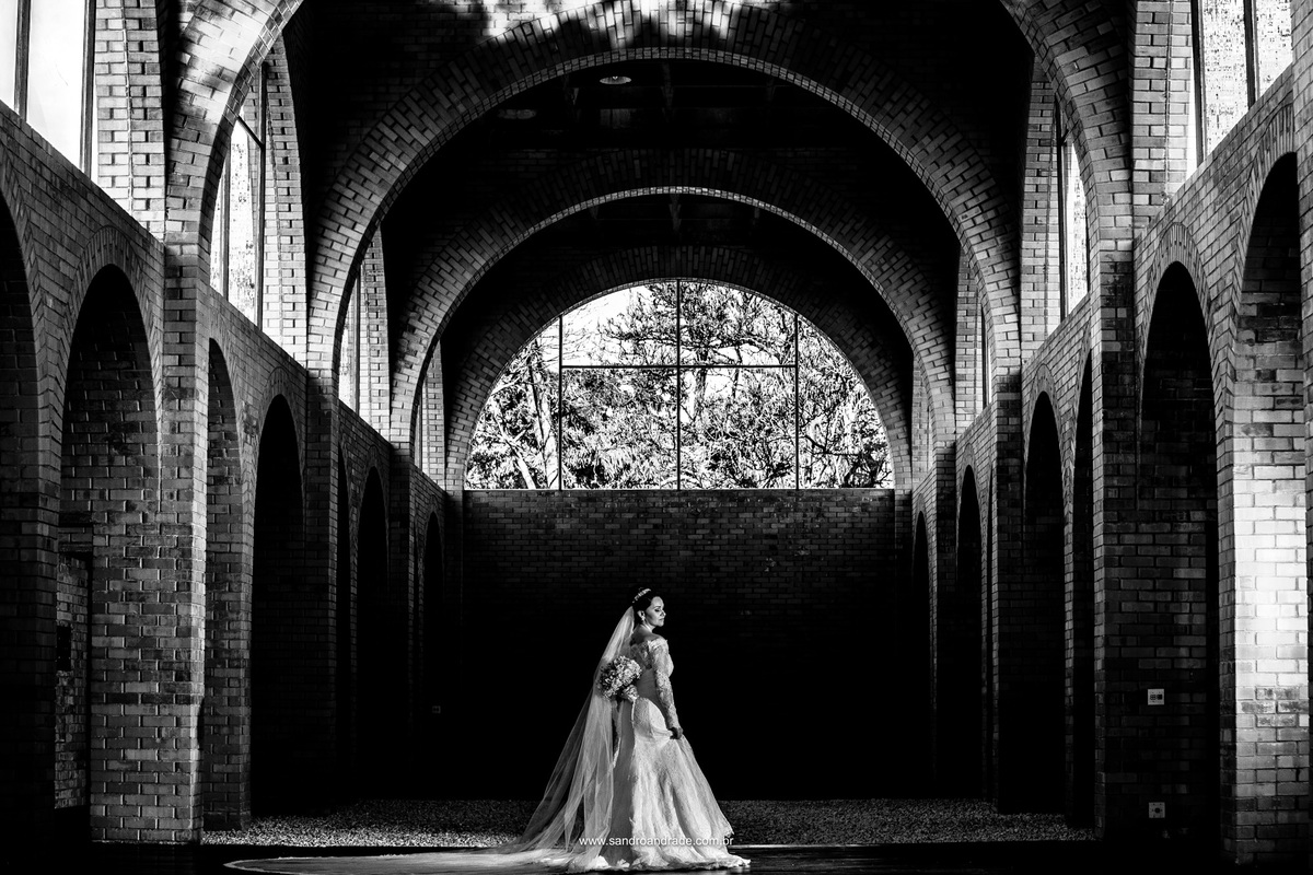 Ela está pronta para o seu tão esperado sim, com um maravilhoso vestido de noiva, buque de flores nobre e um local estonteante nesta fotografia preto e branco.