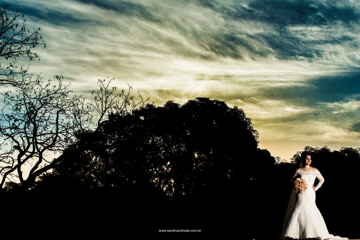 Um lindo céu azul, com um tom amarelado do por do sol e uma noiva linda vestida de branco.