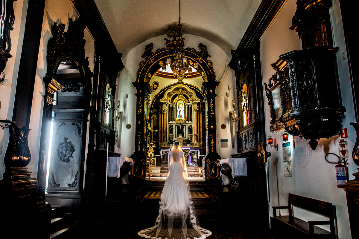 O convento de nossa senhora da penha em vila velha-es é muito lindo, mas com uma noiva no altar é mais lindo ainda. Linda fotografia colorida da noiva de costas no altar do convento.