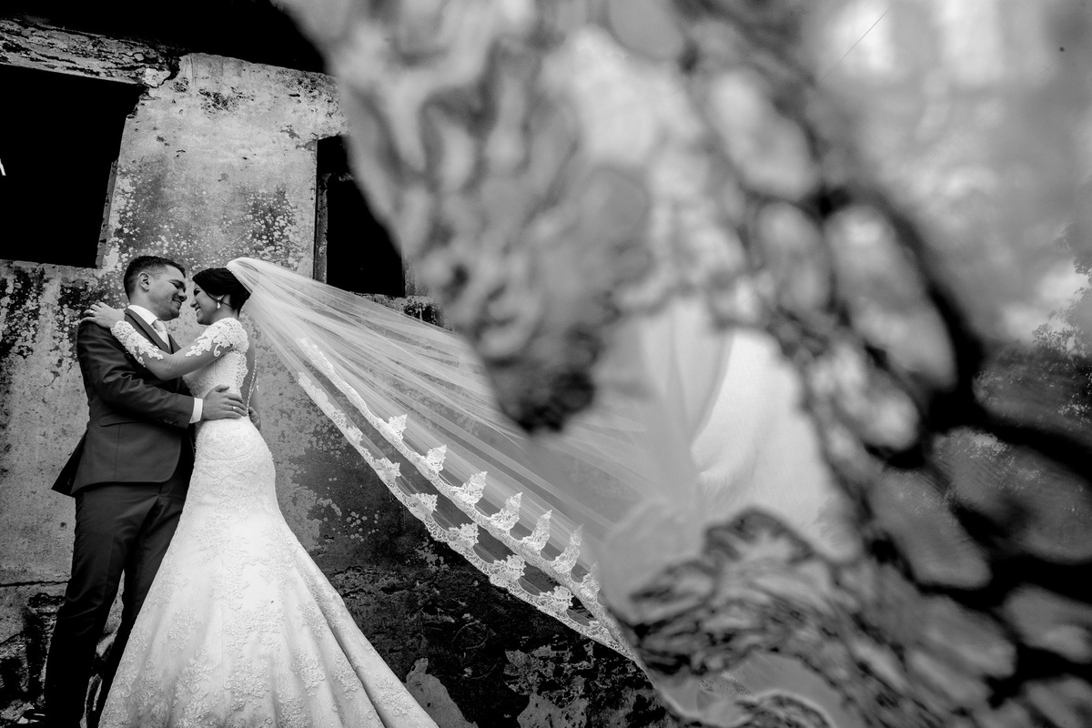 Abraçados e com detalhes do véu, essa fotografia está perfeita em preto e branco.
