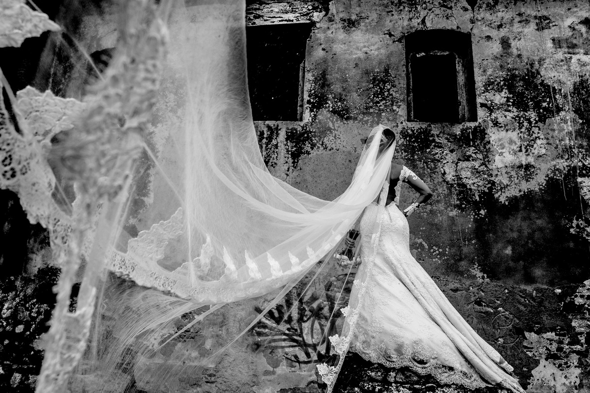 Prteo e branco e uma fotografia de ruinas, com uma noiva linda de costas mostrando detalhes do seu vestido e véu.