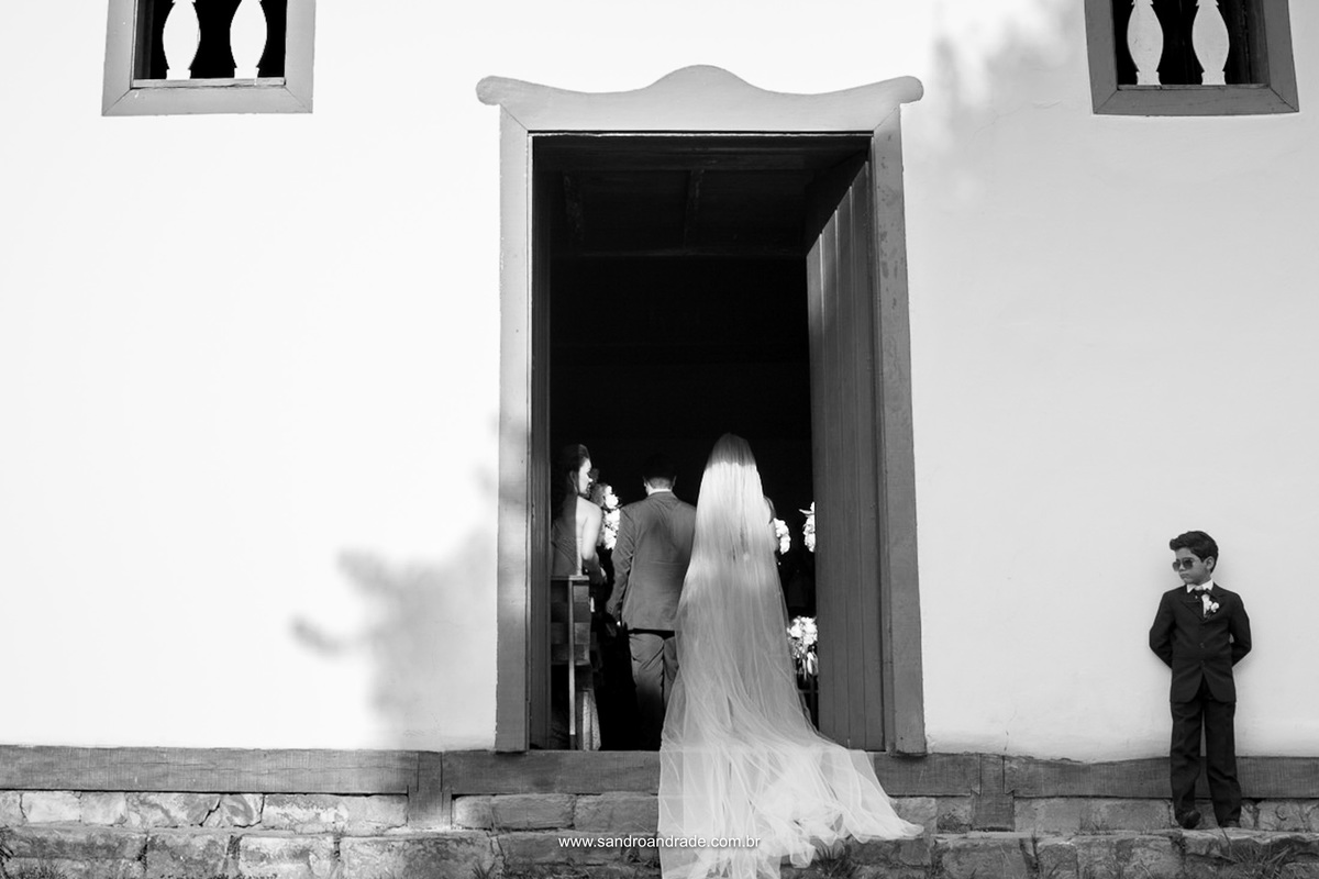 A entrada da noiva, de costas, compondo com a frente da igreja e o menino que entrará com as alianças.